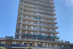 Um edifício residencial com várias andares, varandas, telhado plano e céu claro.