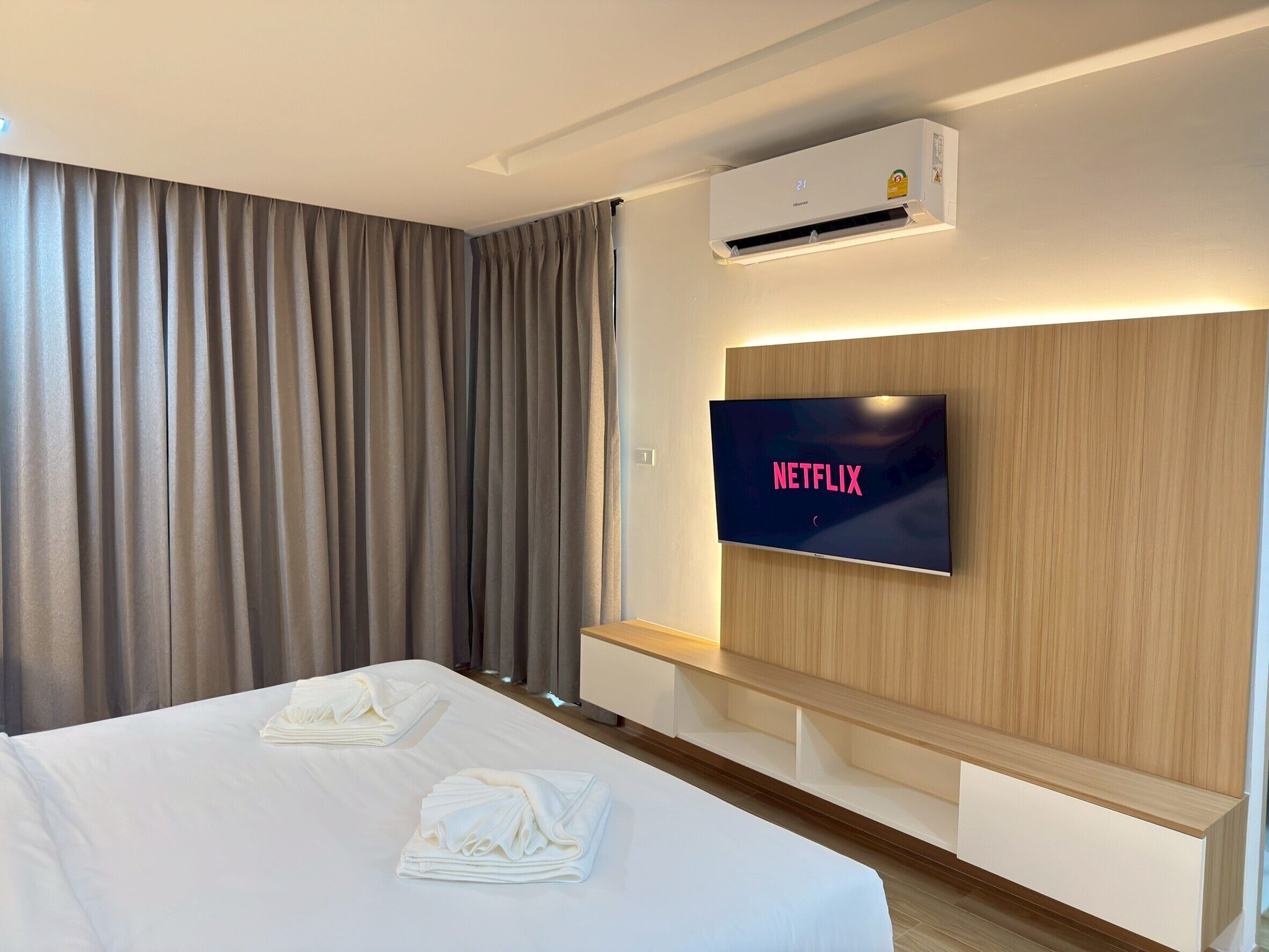 A hotel room with a bed, a TV displaying 'NETFLIX', an air conditioning unit, and a wooden headboard.