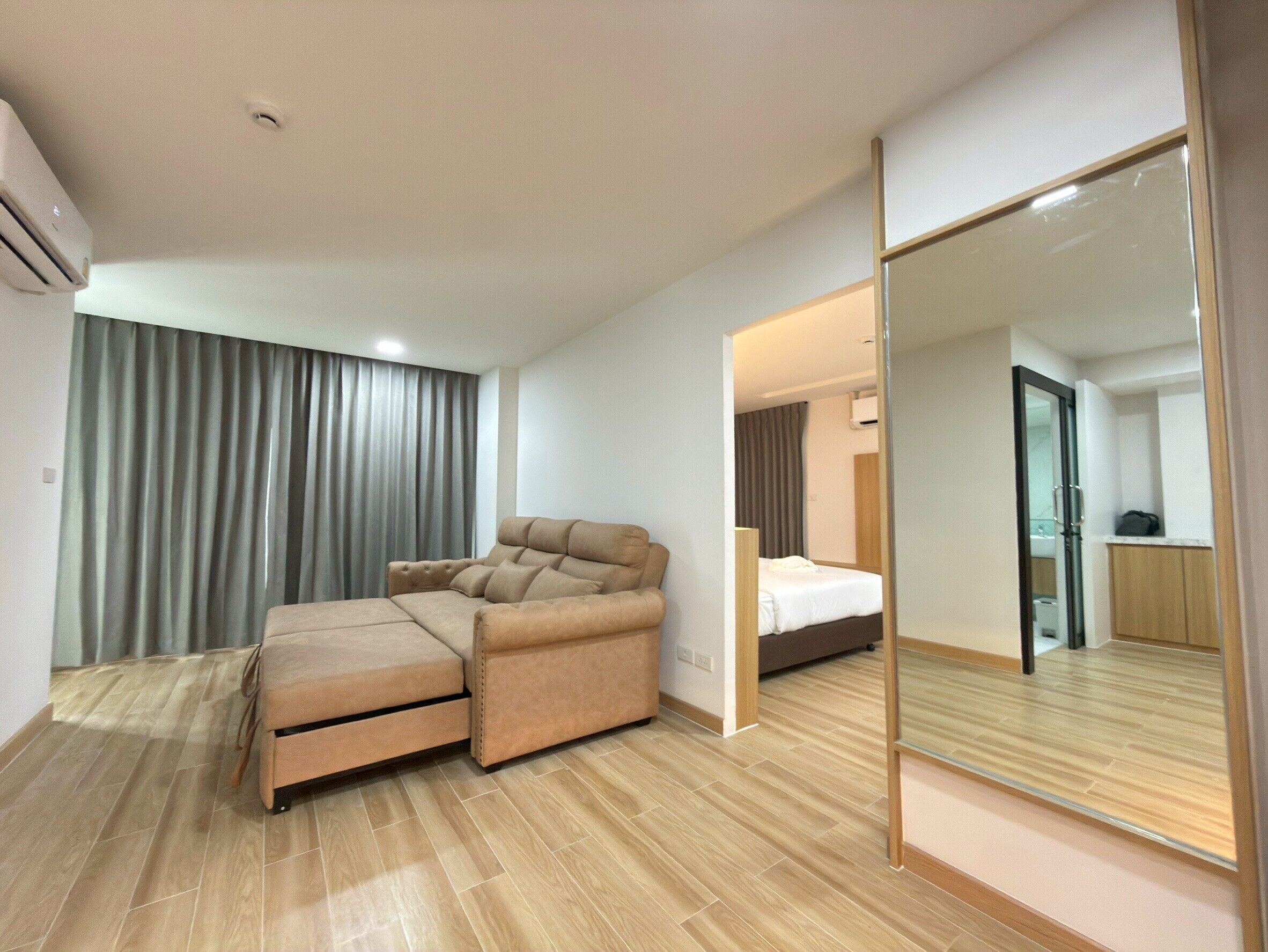 Une chambre d’hôtel moderne avec un canapé, un lit, un miroir et un plancher en bois.