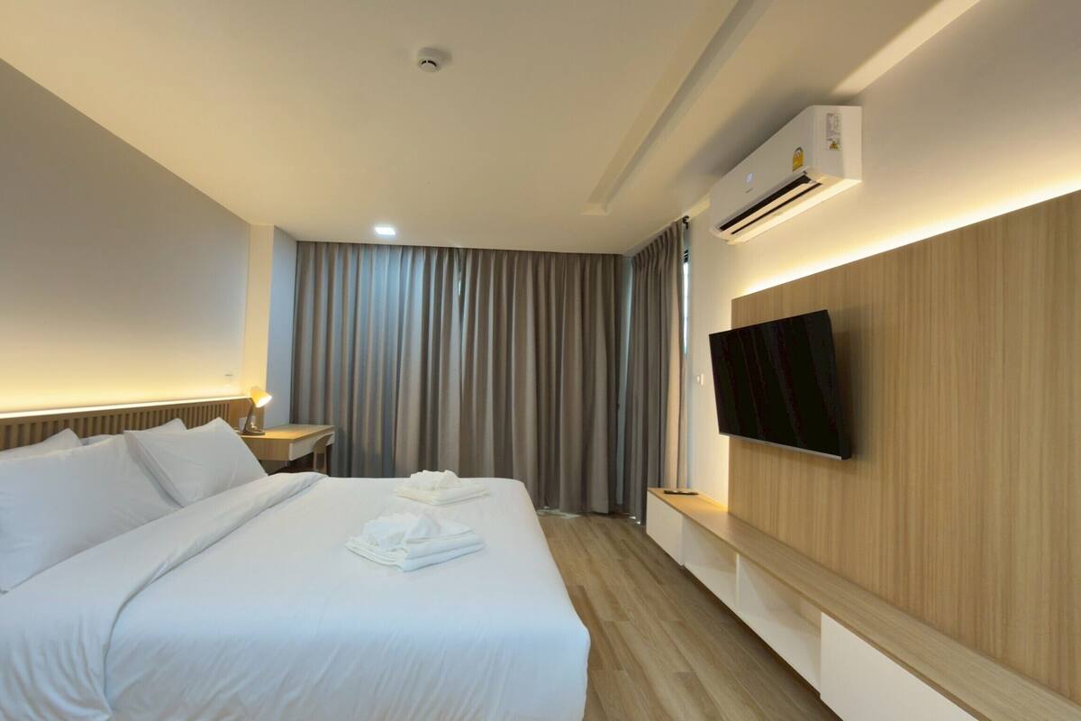 A hotel room with a large bed, a desk, a flat-screen TV mounted on the wall, and an air conditioning unit.