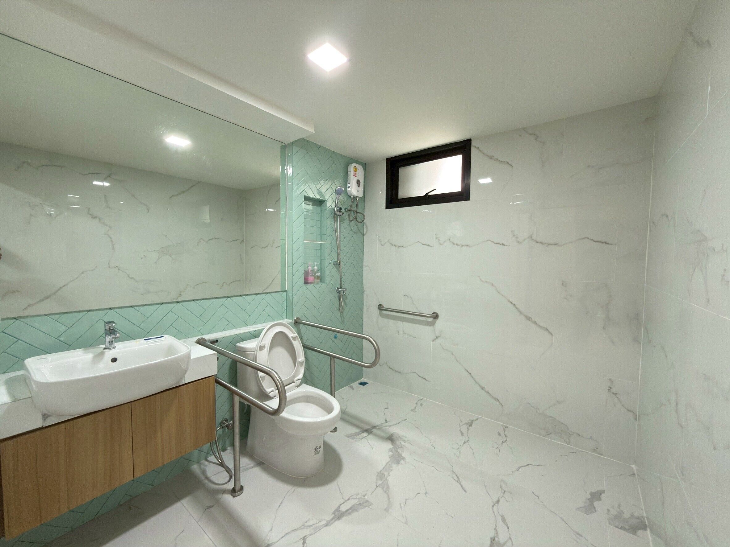 A modern bathroom with a marble floor, a sink, a toilet with a handrail, and a shower area.