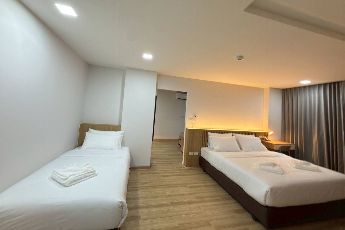 A hotel room with two single beds, a wooden floor, a desk with a lamp, and a view of the hallway.