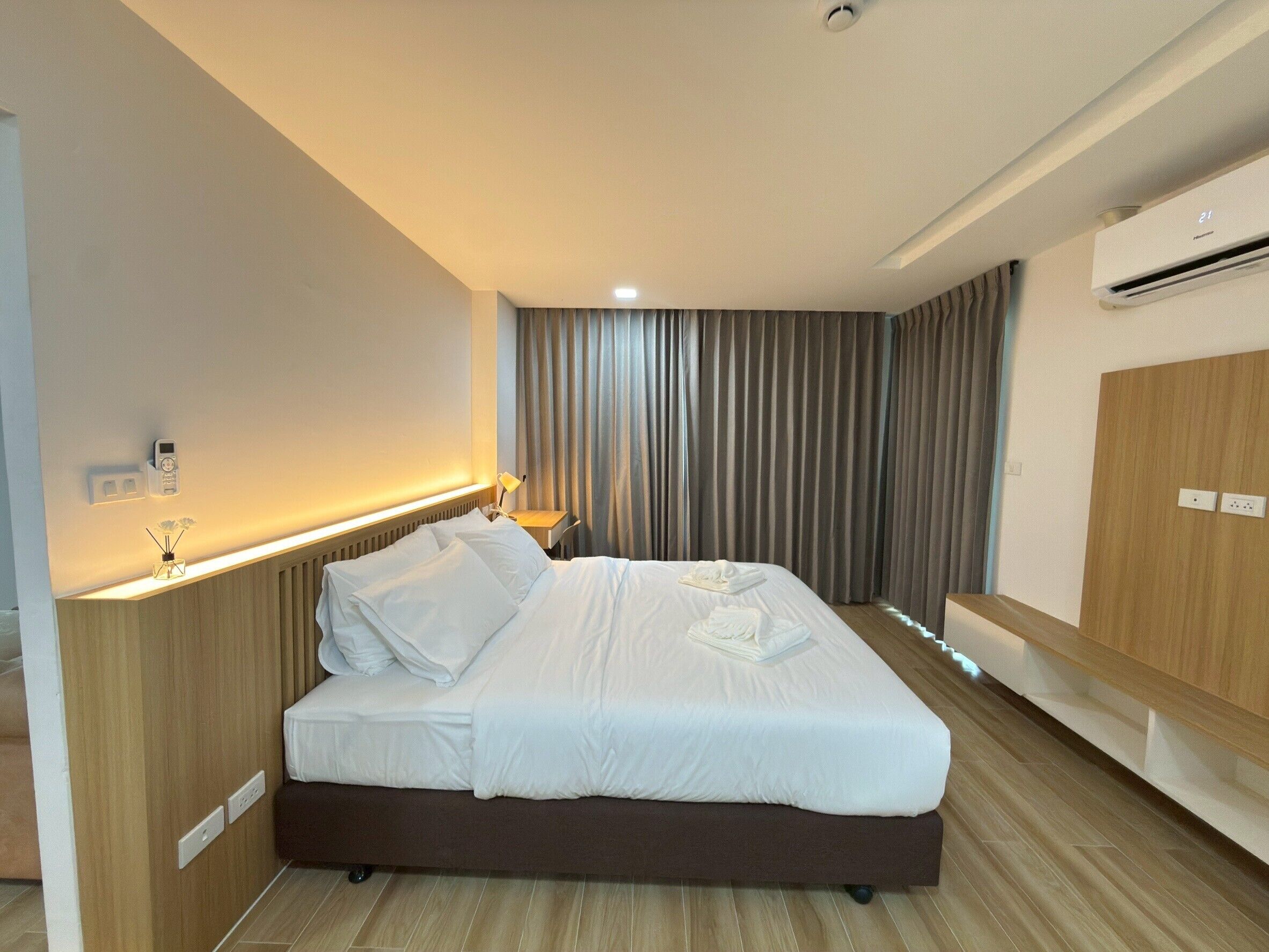 A modern hotel room with a large bed, bedside tables, an air conditioning unit, and a wooden wardrobe.