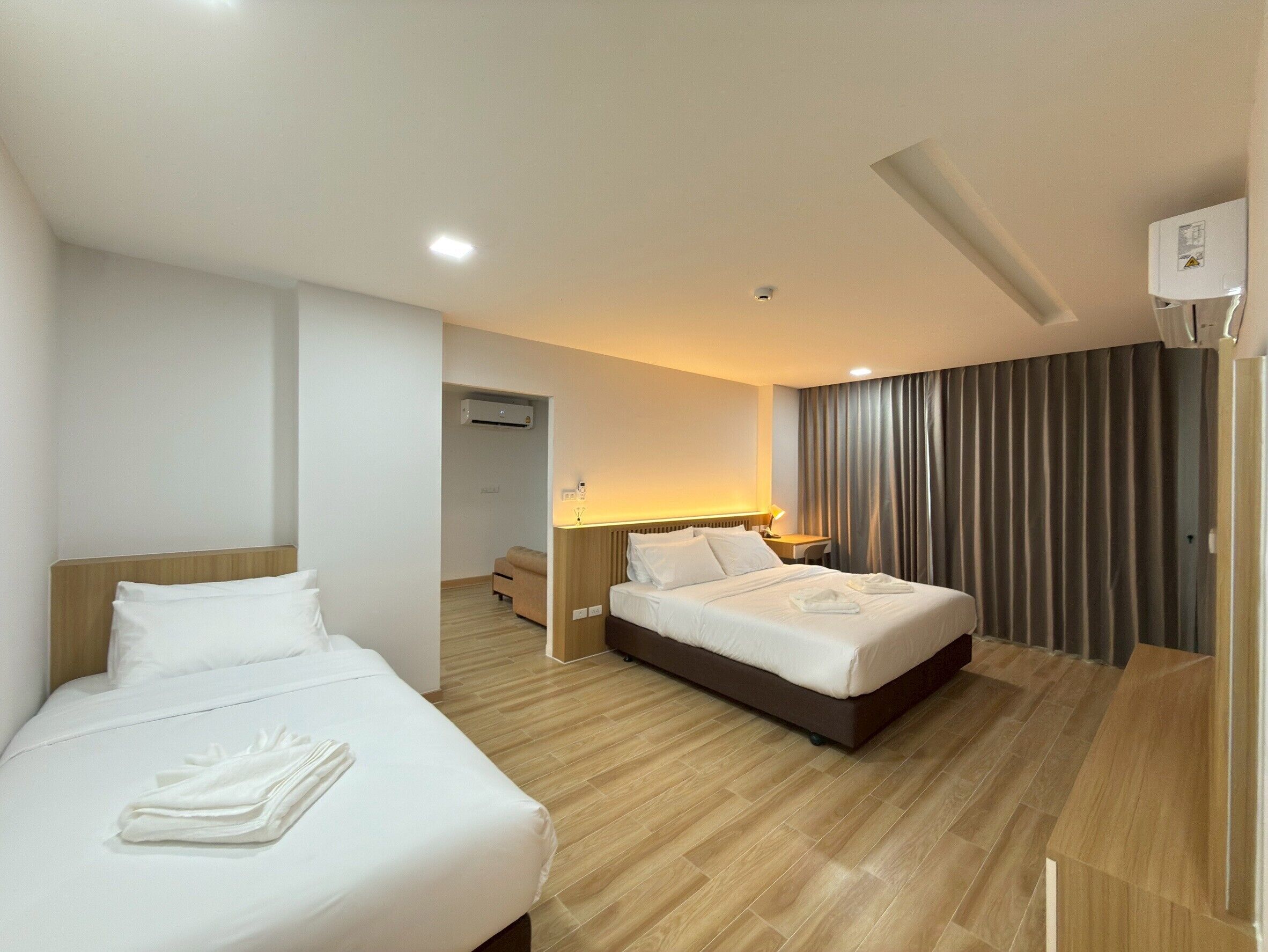 A hotel room with two beds, a desk, a chair, a lamp, and a large window with curtains.