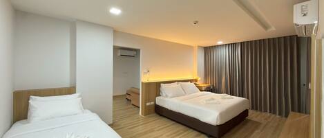 A hotel room with two beds, a desk, a chair, a lamp, and a large window with curtains.