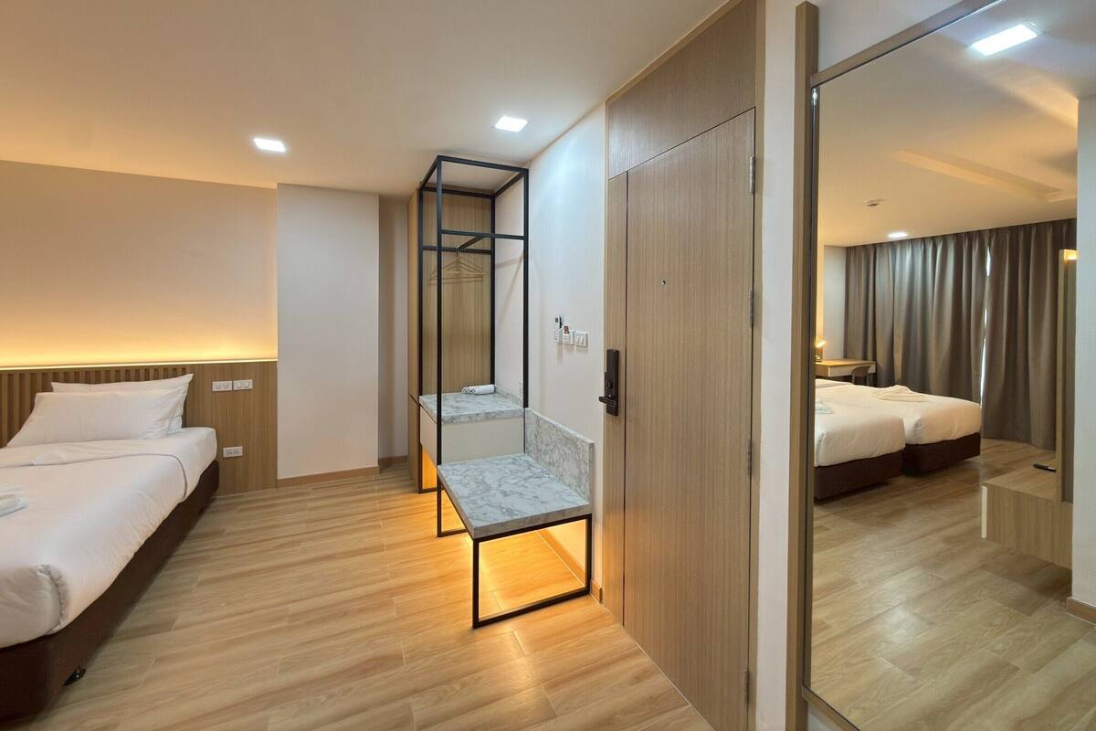 A hotel room with a wooden floor, a bed with white linens, a small table with a marble top, a mirror, and a wardrobe.