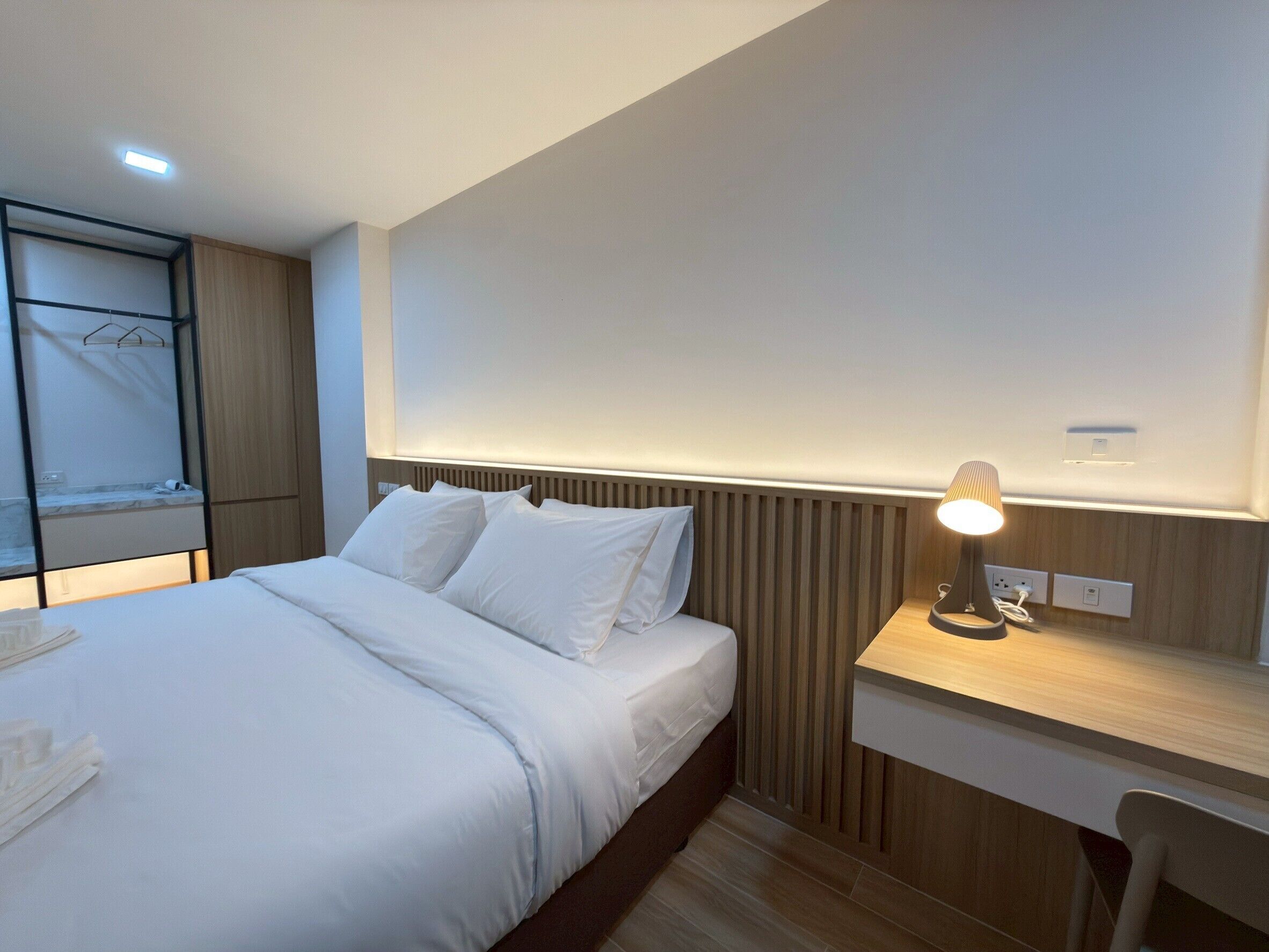 A modern hotel room with a neatly made bed, a bedside table with a lamp, and a built-in wardrobe.