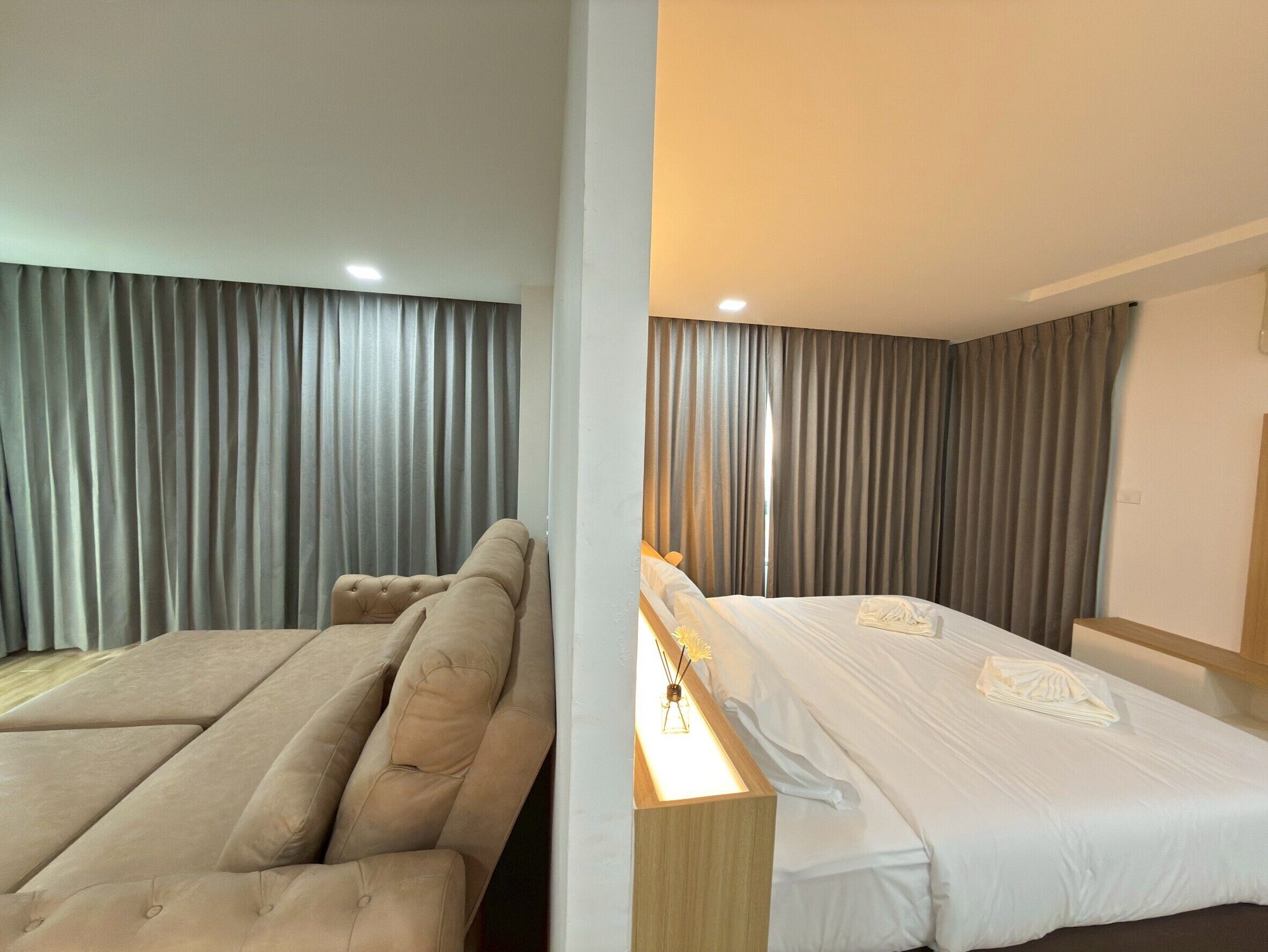 A hotel room with a sofa bed, a single bed, and a bedside table with a lamp.