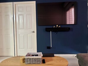 A room with a flat-screen TV mounted on the wall, a wooden coffee table with a remote control, and a wicker storage box.