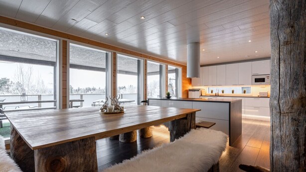 A modern kitchen with a wooden dining table and bench, large windows, and a view of the outdoors.
