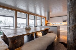 A modern kitchen with a wooden dining table and bench, large windows, and a view of the outdoors.