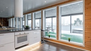 A modern kitchen with large windows, a dining area, and a view of a snowy outdoor deck.