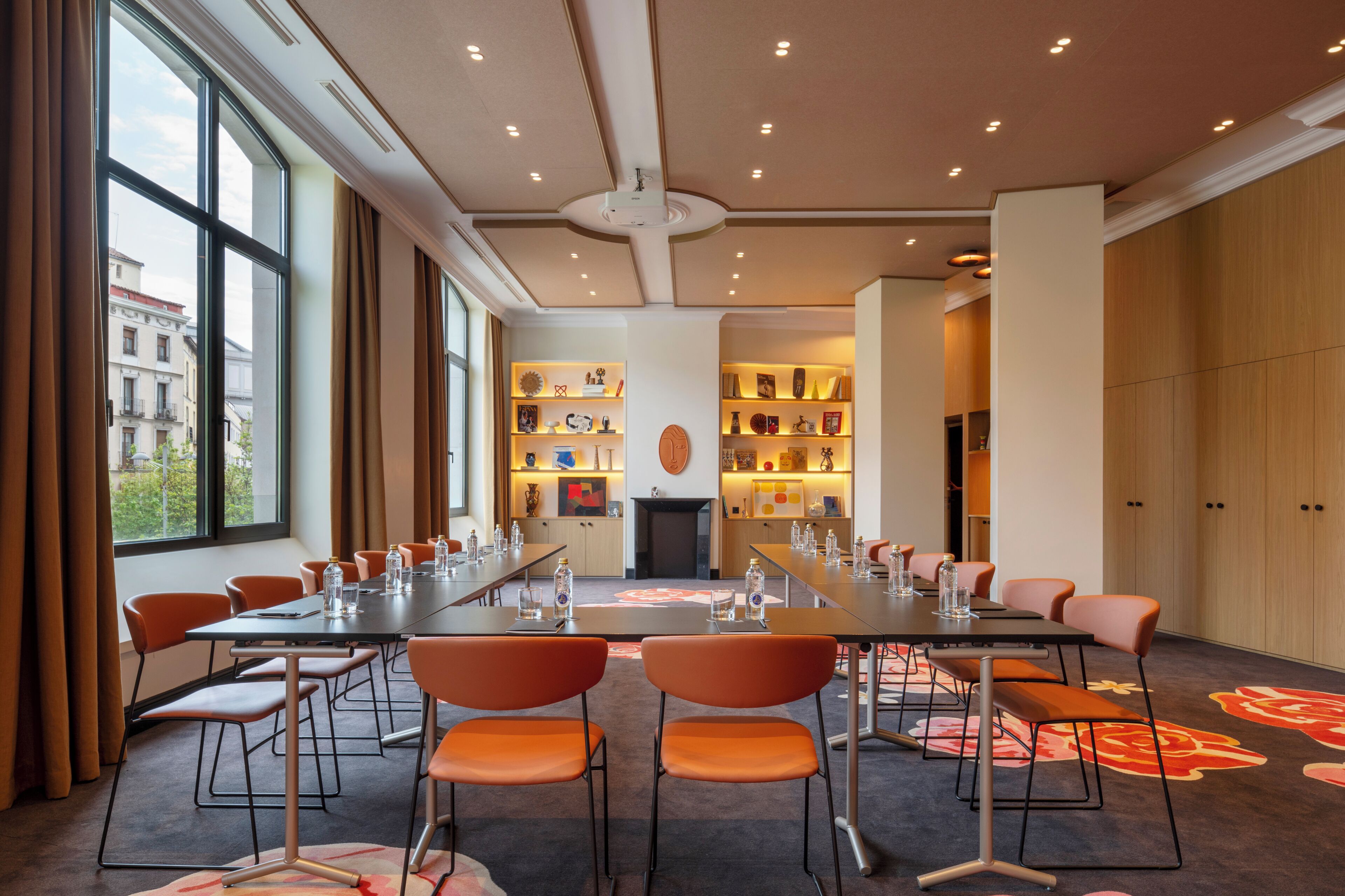 A conference room with a long table, orange chairs, and a carpet with floral patterns.