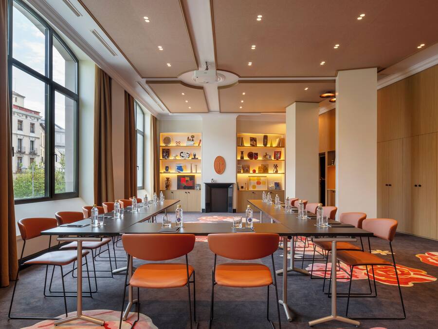 A conference room with a long table, orange chairs, and a carpet with floral patterns.