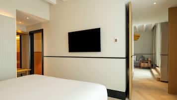 Una habitación de hotel moderna con una cama grande, un televisor de pantalla plana en la pared y un banco de madera en la esquina.