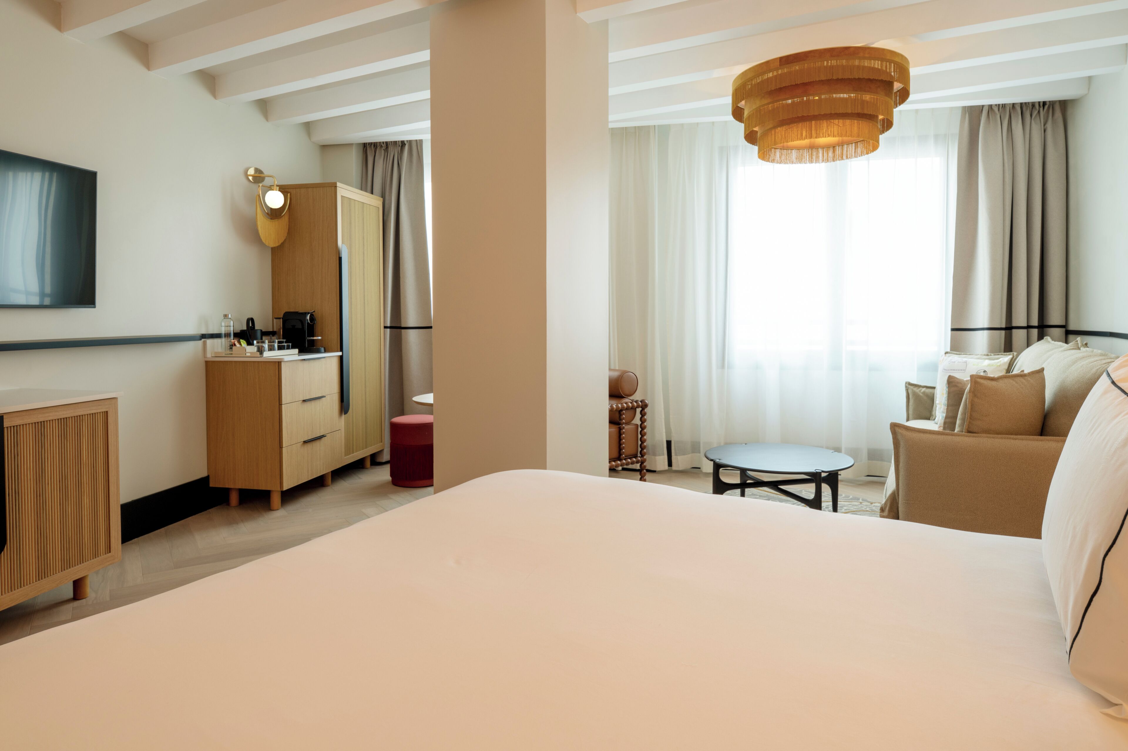 Una habitación de hotel con una cama grande, un escritorio con silla, un armario, una mesita redonda y un televisor montado en la pared.