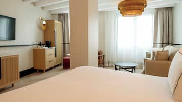 Una habitación de hotel con una cama grande, un escritorio con silla, un armario, una mesita redonda y un televisor montado en la pared.