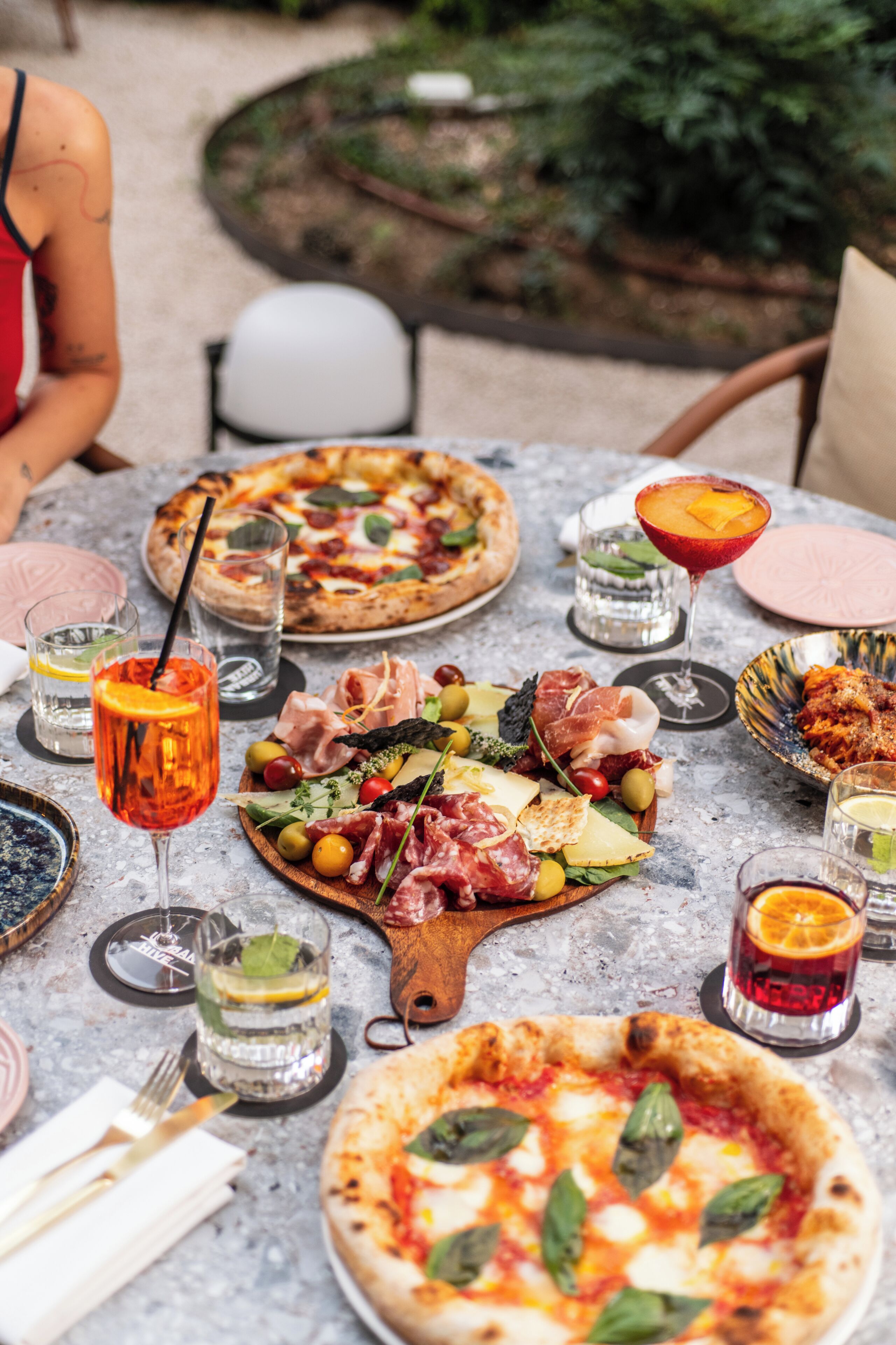 A table set with various food items including pizzas, a charcuterie board, and drinks.