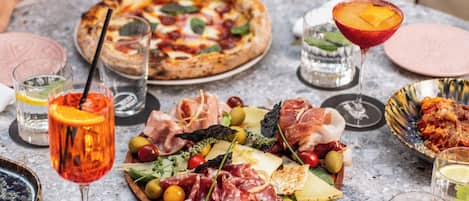 A table set with various food items including pizzas, a charcuterie board, and drinks.