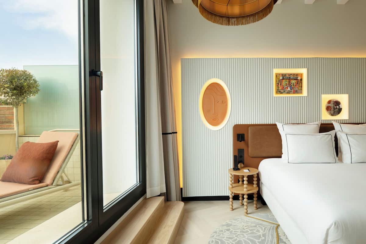 Ein Hotelzimmer mit großem Fenster, einem Bett, einem kleinen Tisch und einem an der Wand befestigten Kunstwerk.