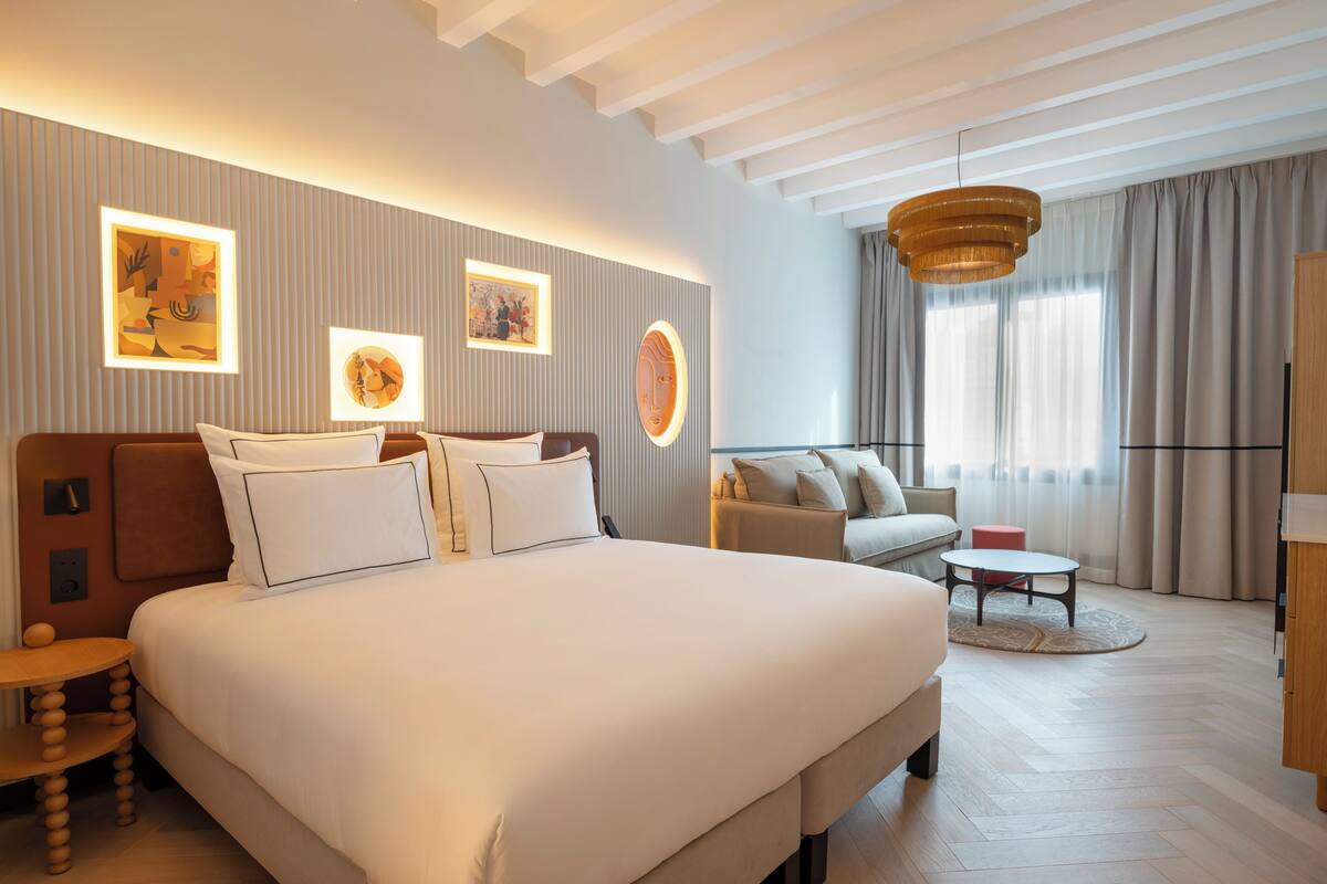 Ein modernes Hotelzimmer mit einem großen Bett, einer Couch, einem kleinen Tisch und Kunstwerken an den Wänden.