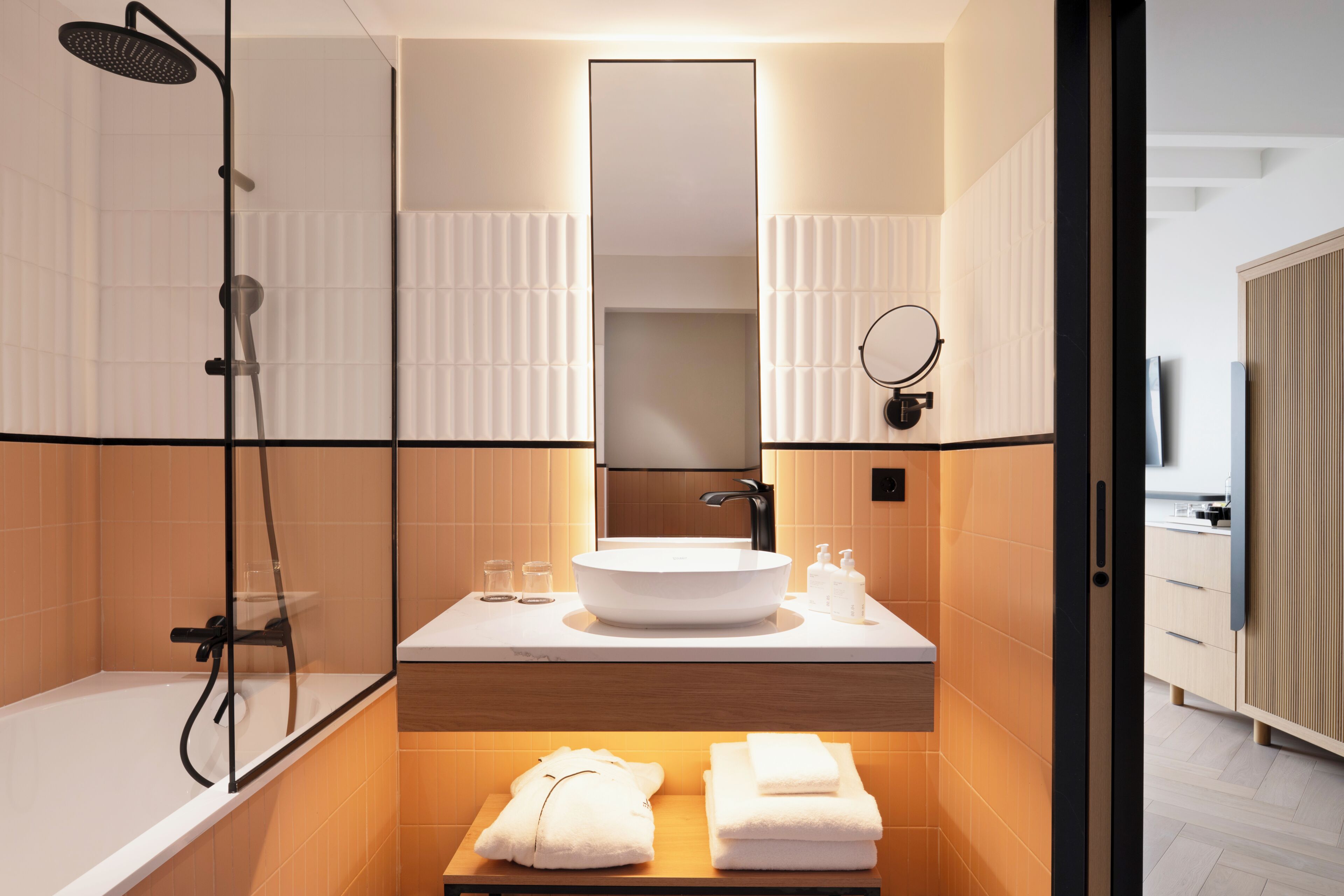 A modern bathroom with a bathtub, a large mirror, a round sink, and a shower.
