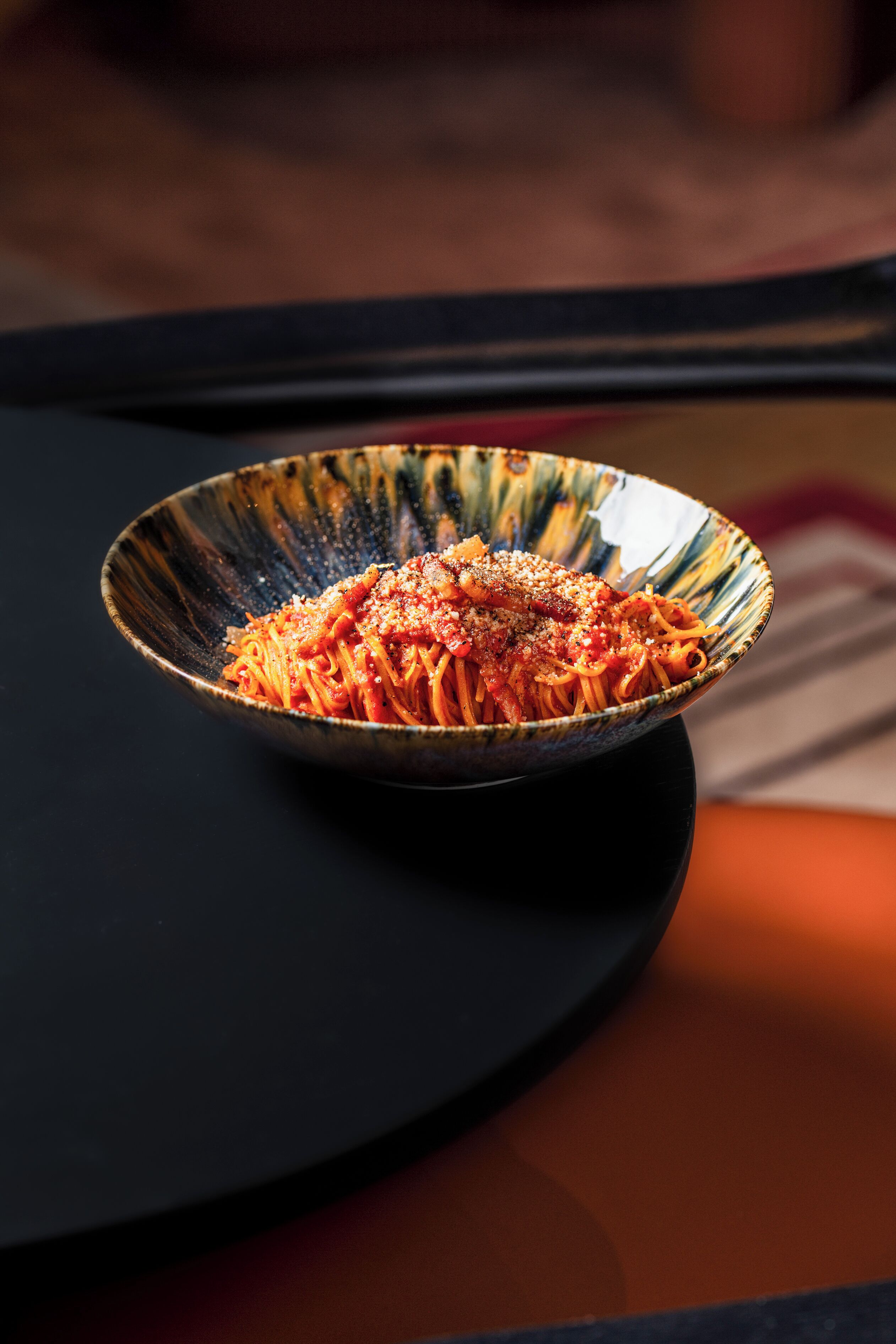 A bowl of spaghetti with a glossy finish, placed on a dark surface.