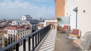 Ein Balkon mit Korbstühlen und einem kleinen Tisch, mit Blick auf eine Stadtlandschaft mit historischen Gebäuden und einer Kuppel.