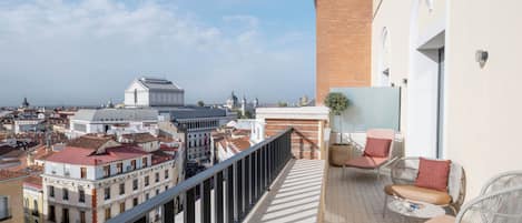 Un balcón con sillas de mimbre y una pequeña mesa, con vistas a un paisaje urbano que incluye edificios históricos y una estructura en forma de cúpula.