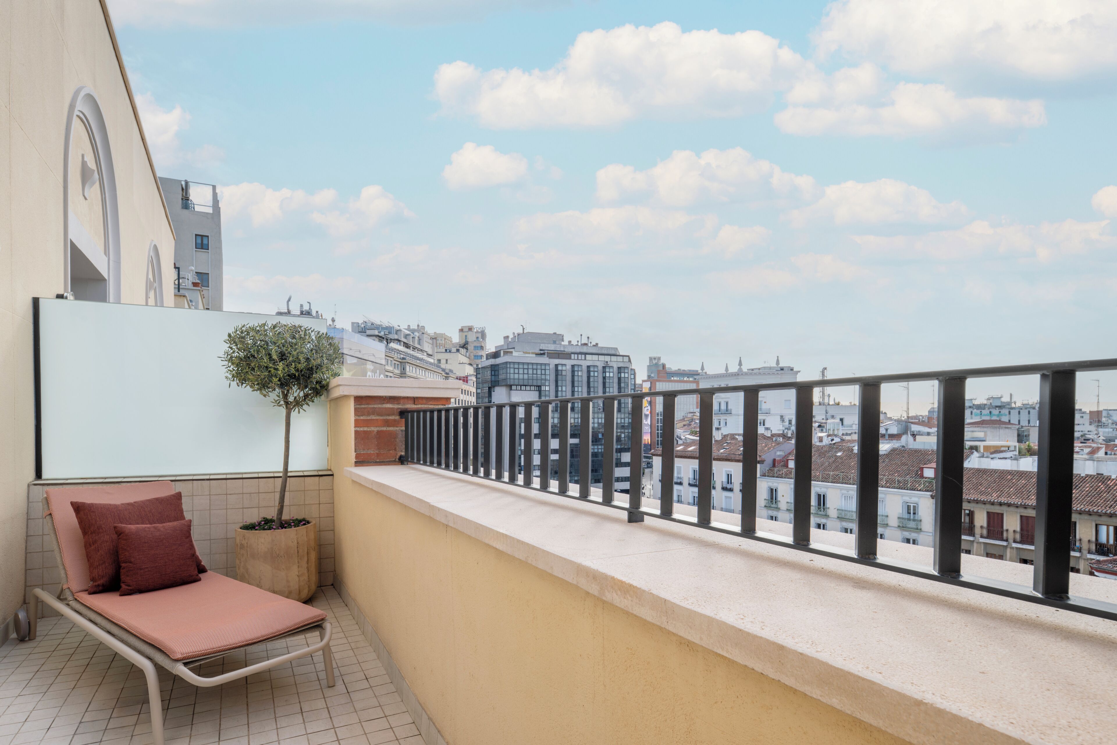 A balcony with a bed, a potted plant, and a view of the cityscape.