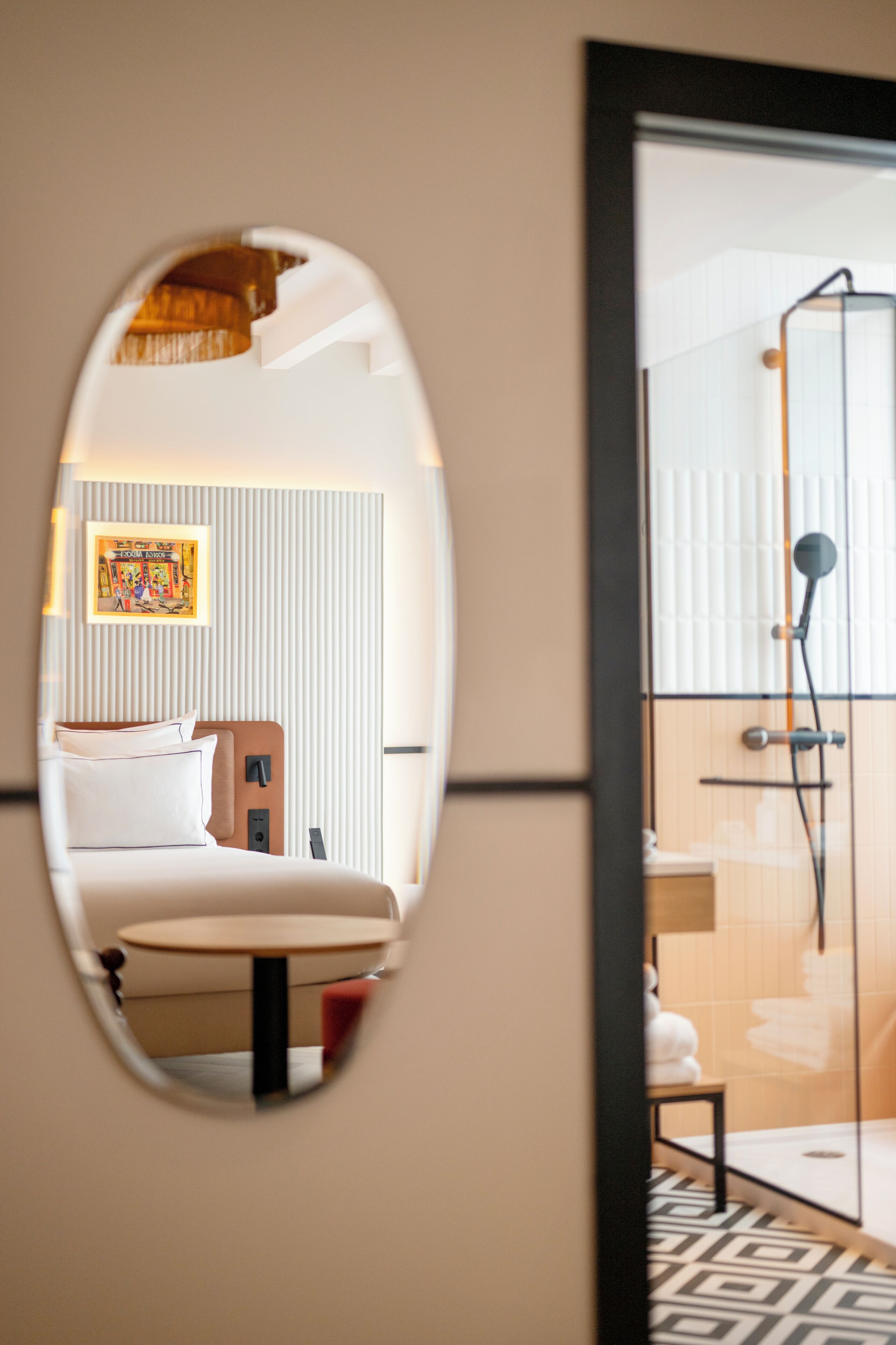 A hotel room with a bed, a small table, a shower area, and a mirror reflecting the room.