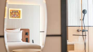 A hotel room with a bed, a small table, a shower area, and a mirror reflecting the room.