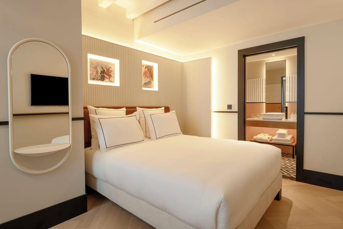 Ein Hotelzimmer mit einem Bett, einem Fernseher, einem Spiegel und einem durch eine geöffnete Tür einsehbaren Badezimmer.