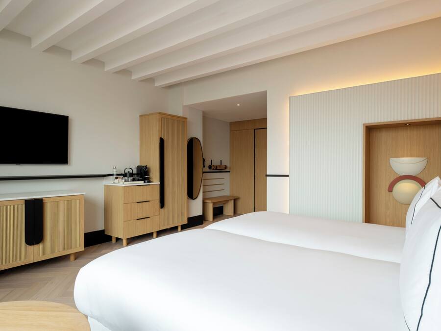 Una habitación de hotel moderna con una cama grande, muebles de madera, un televisor de pantalla plana y un aplique fijado a la pared.