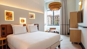 Ein Hotelzimmer mit einem großen Bett, einem Schreibtisch, einem Sessel, einem Fernseher und Bildern an den Wänden.