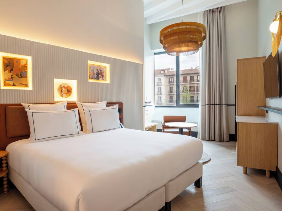 Habitación de hotel con una cama grande, escritorio, silla, televisor y obras de arte en las paredes.