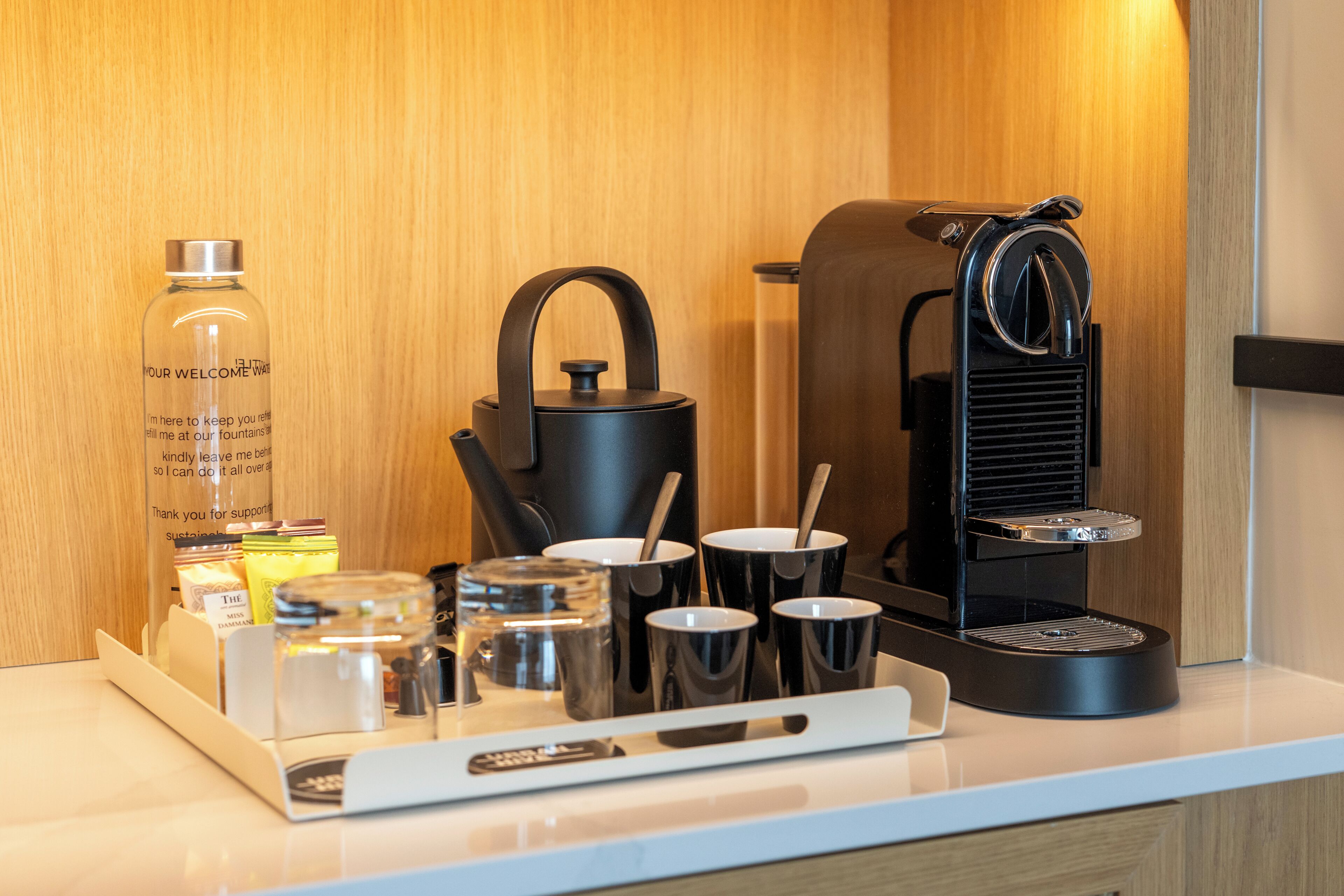 Una estación de café con una tetera, tazas y una botella de agua en una habitación de hotel.