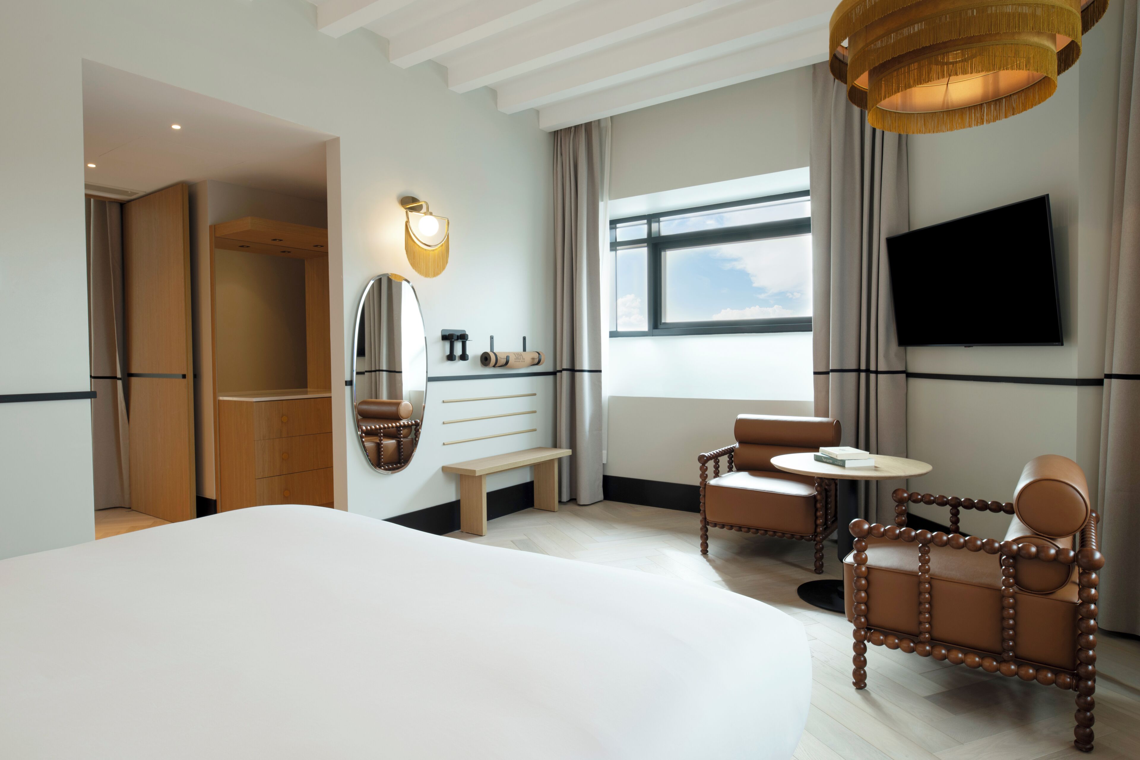 A hotel room with a large bed, a seating area with two chairs, a television mounted on the wall, and a window with a view.