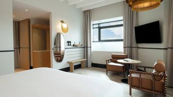 A hotel room with a large bed, a seating area with two chairs, a television mounted on the wall, and a window with a view.