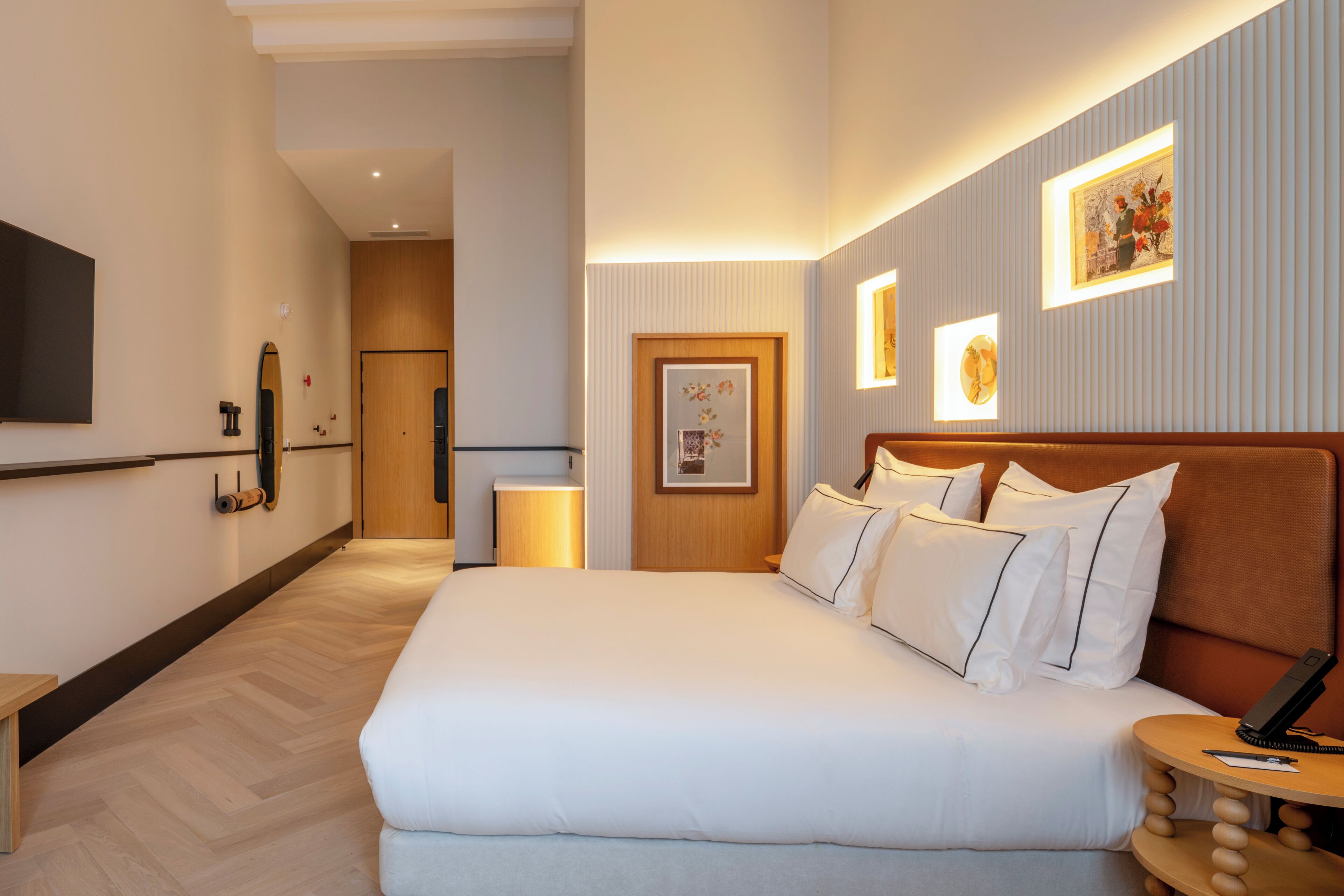 Una camera d'albergo con un letto grande, comodini, una TV a schermo piatto e opere d'arte incorniciate alle pareti.