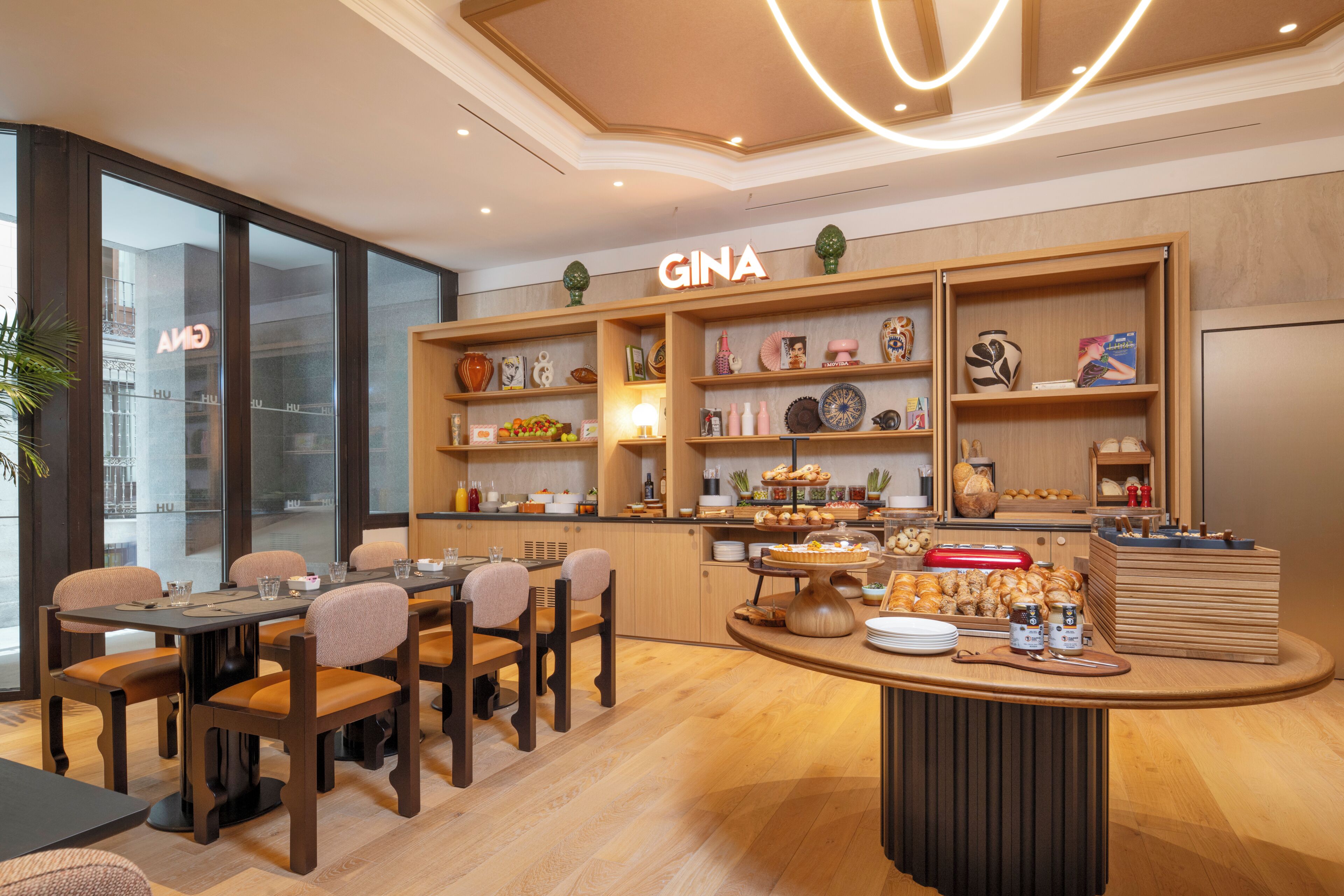 Restaurante GINA con una decoración moderna, que incluye un área de comedor central con mesas y sillas de madera, un mostrador con diversos alimentos y estantes con objetos decorativos.