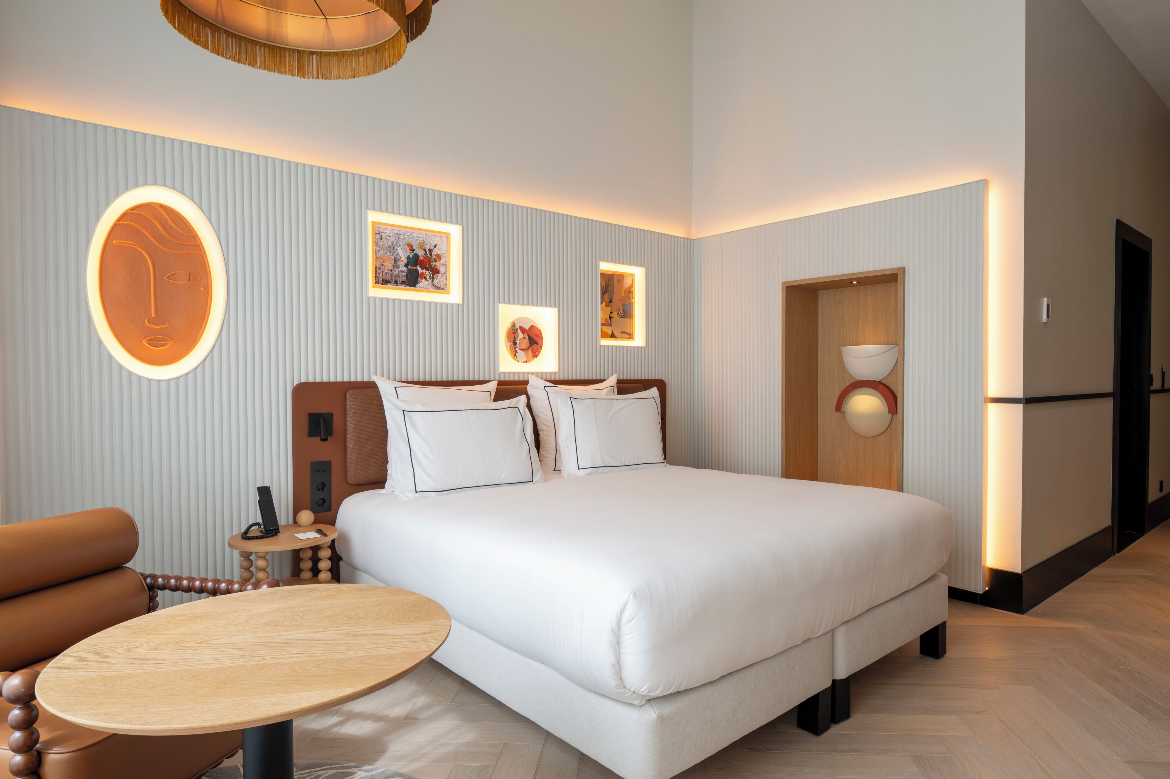 Een hotelkamer met een groot bed, een ronde houten tafel, een bank en een muur met ingelijste foto's.