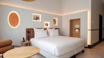 Habitación de hotel con una cama grande, una mesa redonda de madera, un sofá y una pared decorada con cuadros.