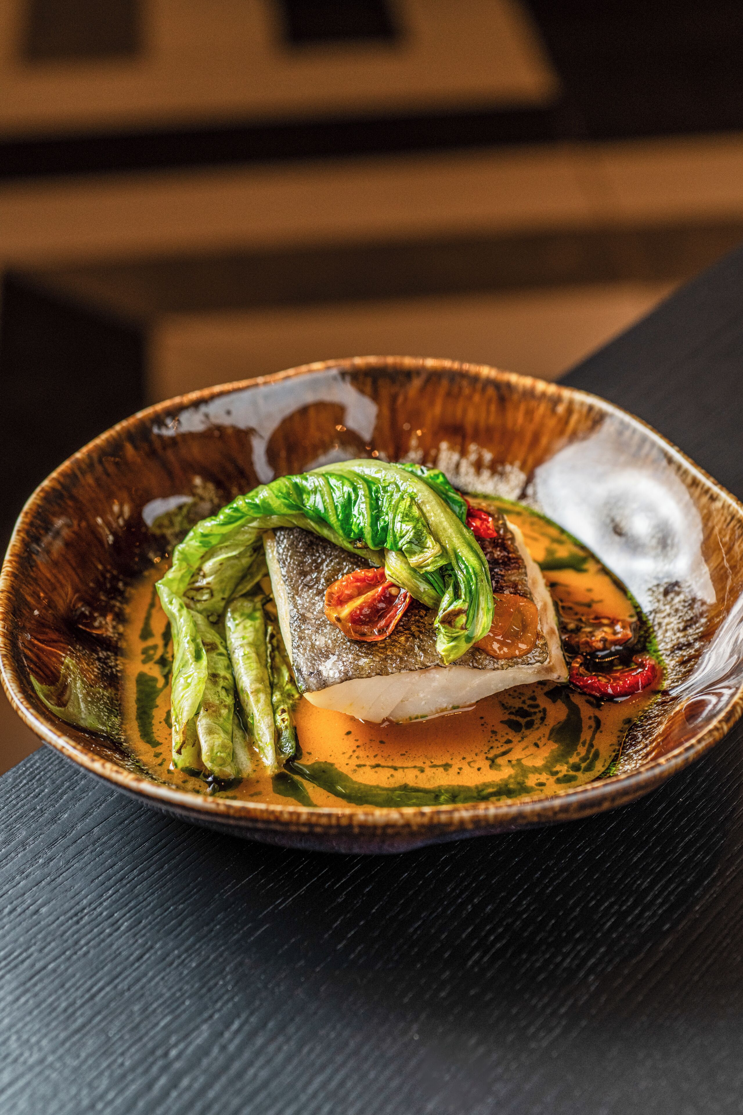 Ein Teller mit Fisch, grünen Gemüsesorten und roten Chilischoten.
