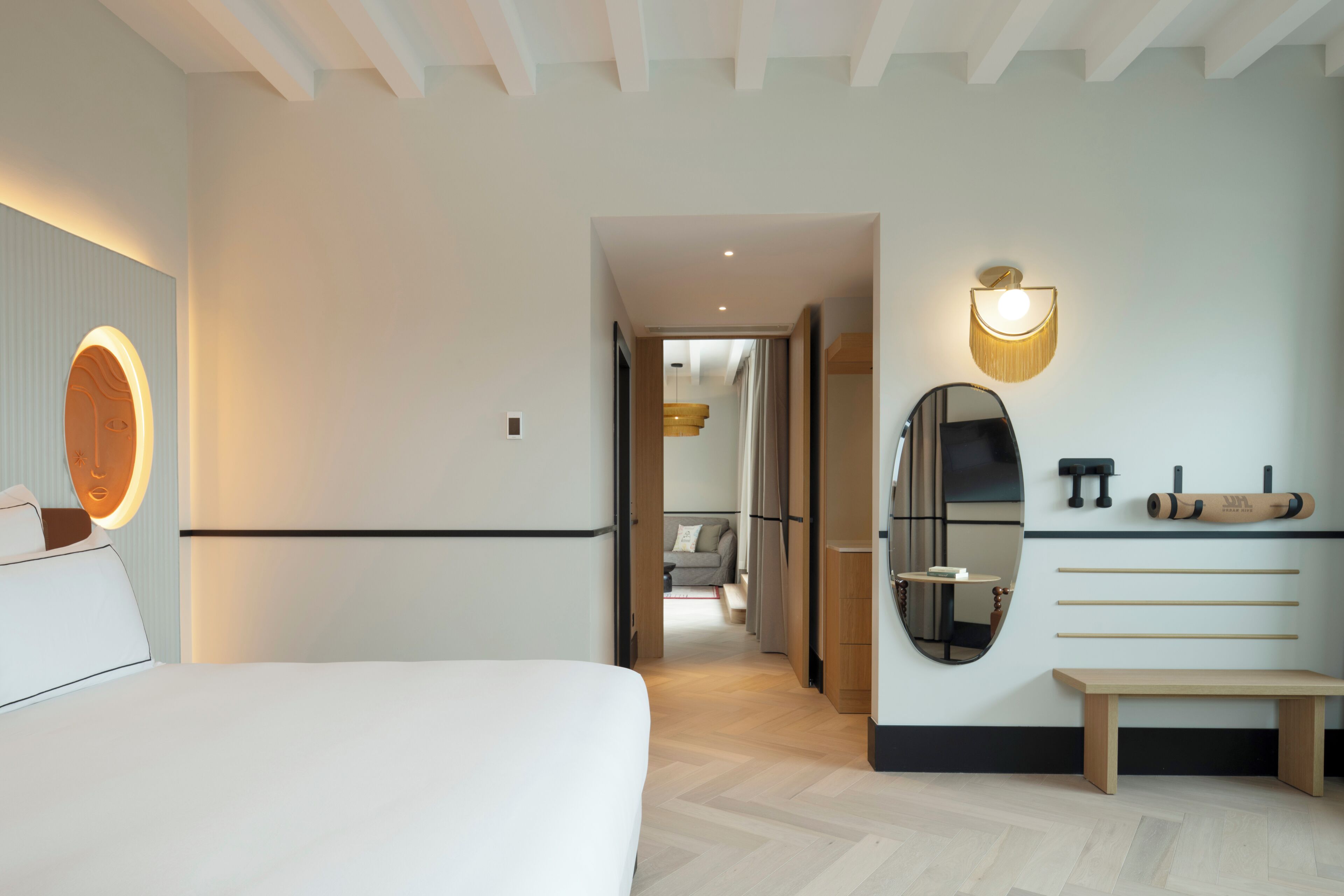 Una habitación de hotel moderna con cama, mesita de noche, espejo, toallero en la pared y un banco.