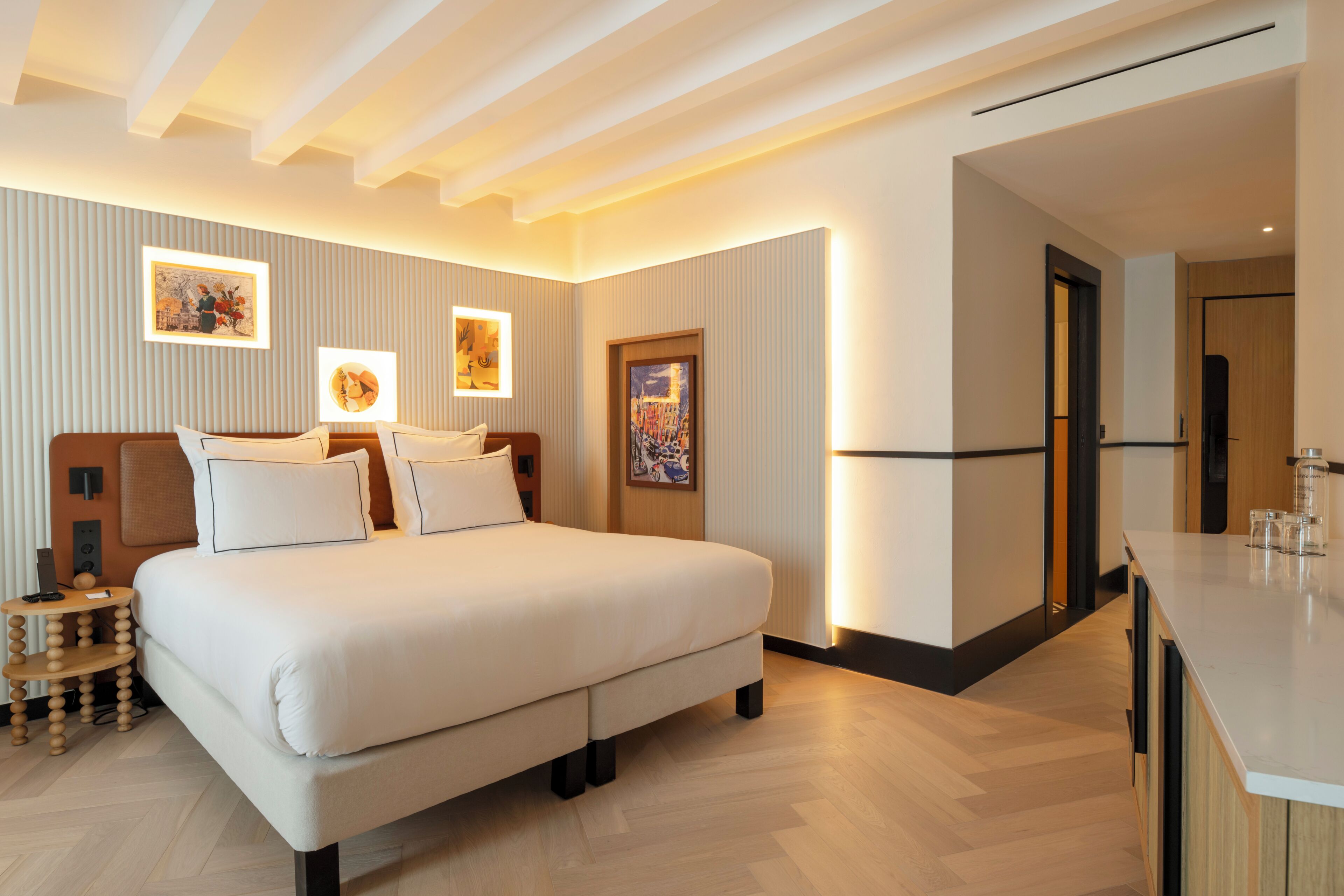 Una habitación de hotel moderna con una cama grande, mesitas de noche, un escritorio y obras de arte en las paredes.