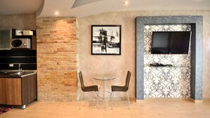 Een moderne keuken met een ingebouwde magnetron, een zithoek met twee stoelen, een tafel en een flatscreen-tv bevestigd aan een decoratieve muur.