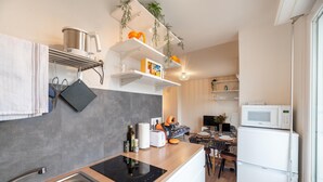 Eine moderne Küche mit Einbauherd, Mikrowelle und Kühlschrank. Über der Arbeitsplatte befinden sich Regale mit verschiedenen Küchenutensilien und Pflanzen.