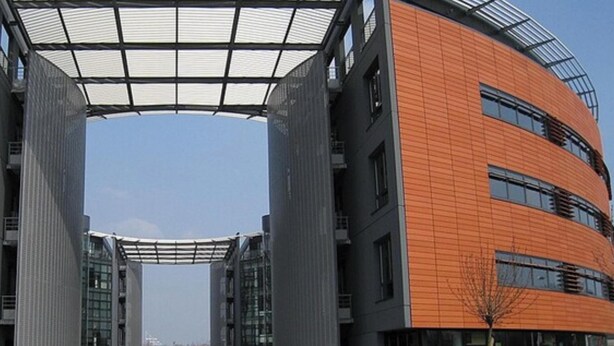Ein modernes Gebäude mit einer zentralen Glasstruktur und gewölbten, orangefarbenen Wänden.