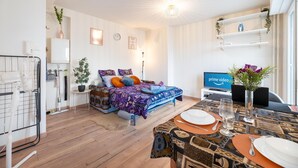 Ein moderner, gut beleuchteter Raum mit einem Bett, einem Esstisch für zwei Personen und einem Fernseher, der 'Prime Video' anzeigt.
